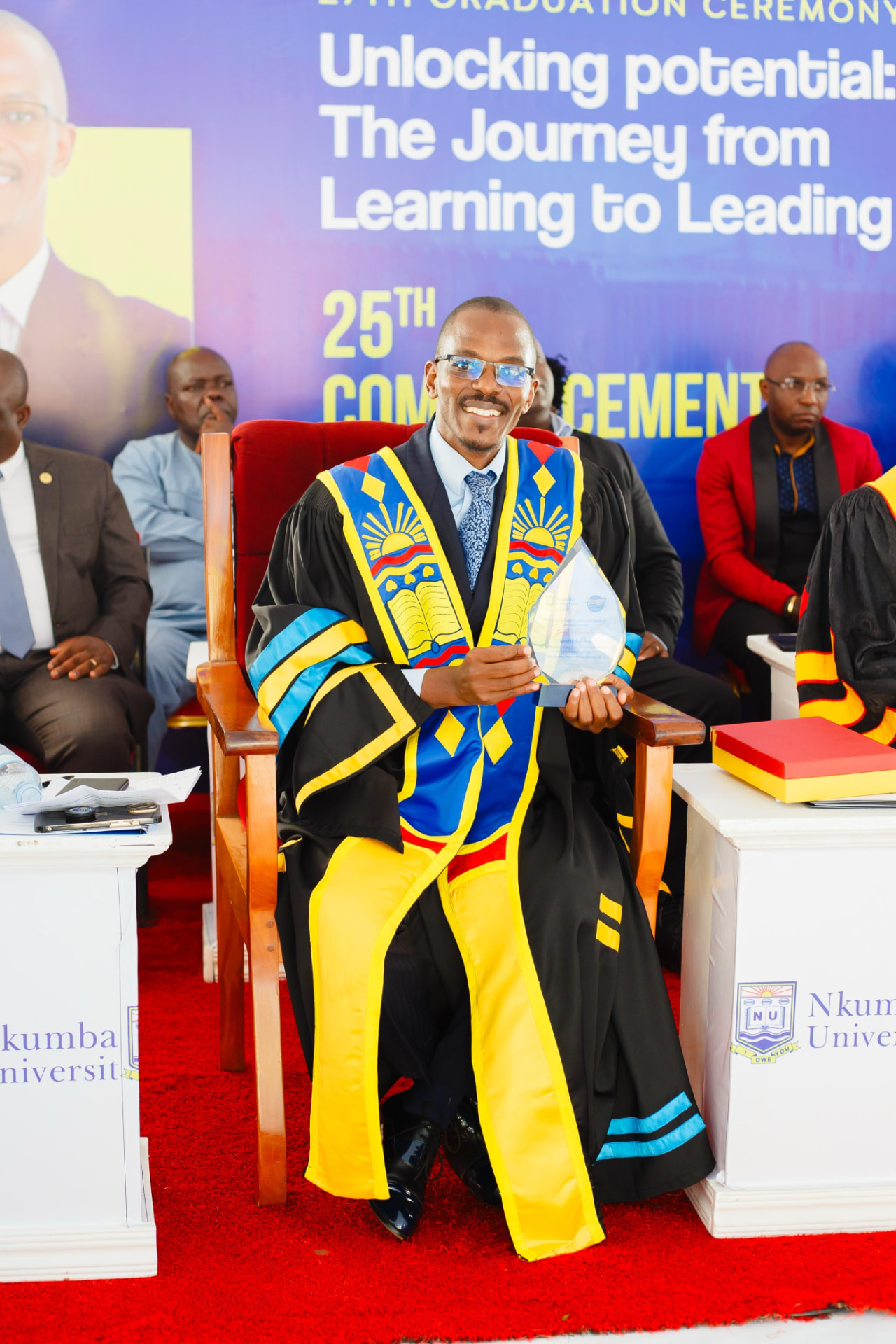 Newton Buteraba seated with an award at a commencement