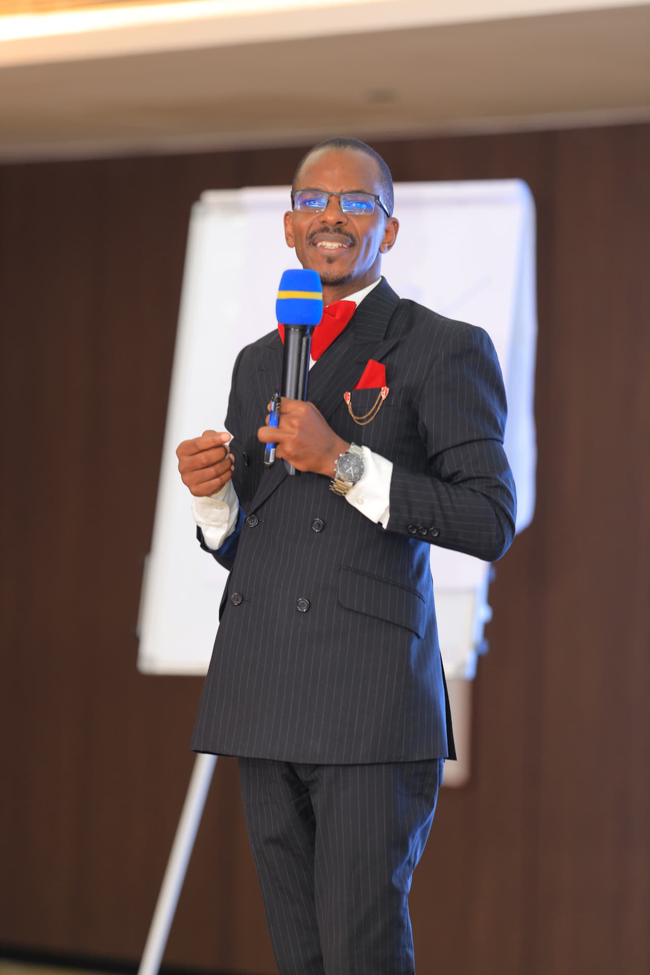 Newton Buteraba speaking with a microphone in a pinstripe suit